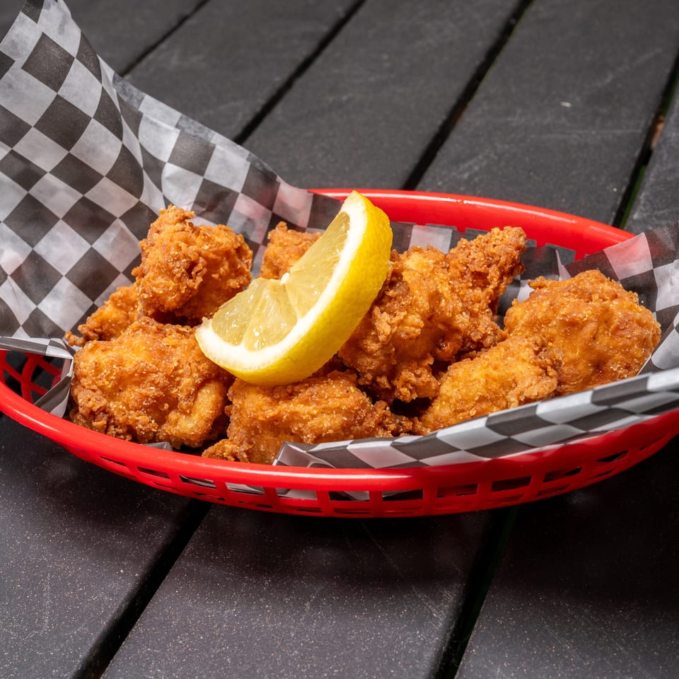 Golden fried chicken bites with a lemon wedge in a red basket lined with checkered paper.