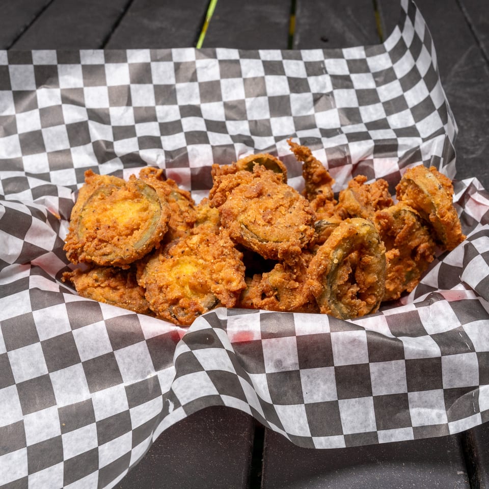 A basket of crispy fried pickles in a black and white checkered paper liner on a dark table.