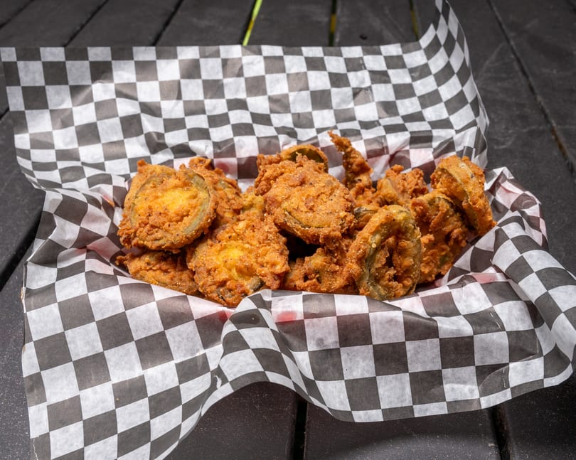 A basket of crispy fried pickles in a black and white checkered paper liner on a dark table.