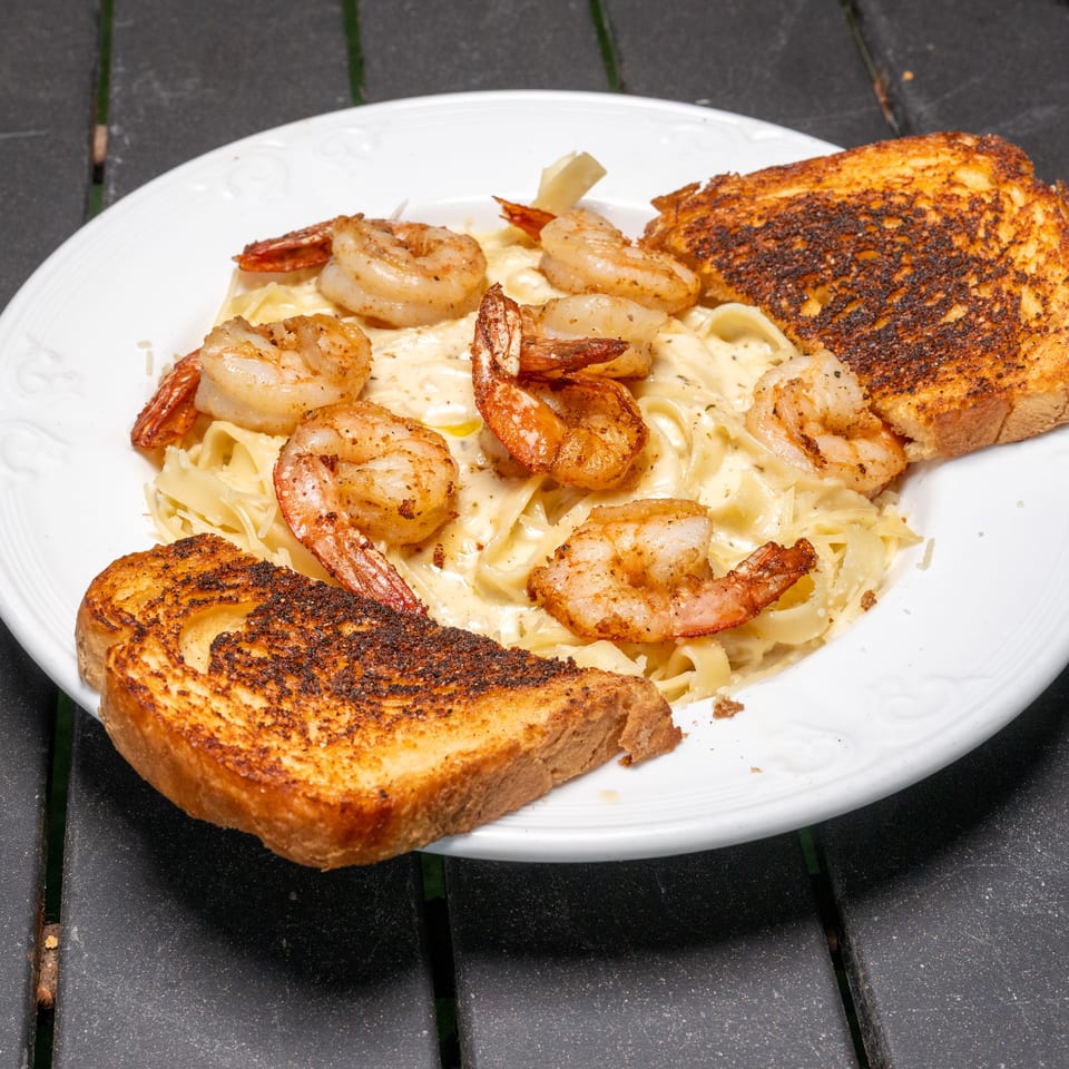 Shrimp alfredo pasta with two slices of toasted garlic bread on a white plate.