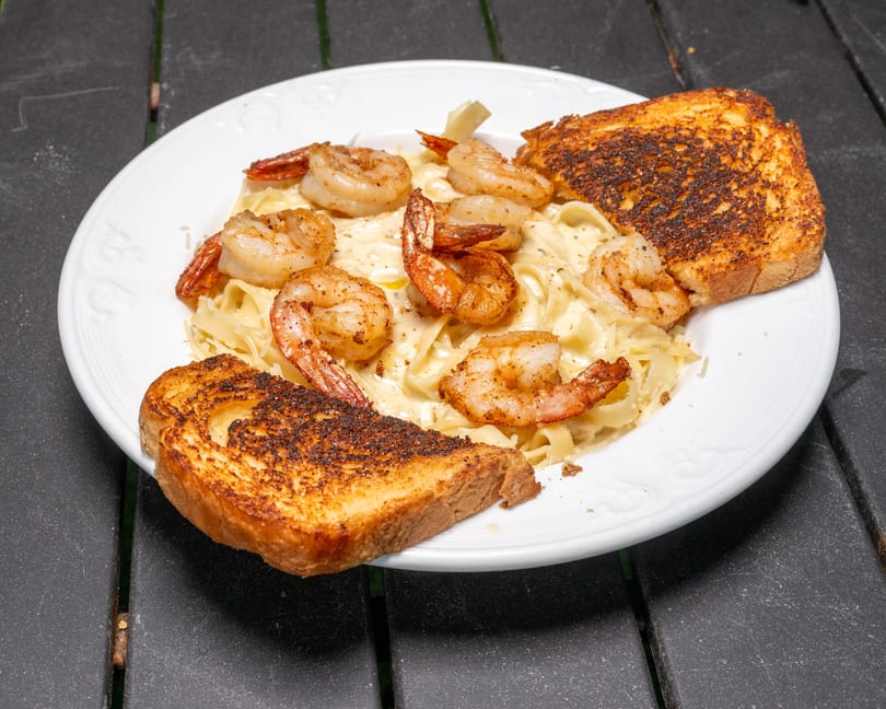 Shrimp alfredo pasta with two slices of toasted garlic bread on a white plate.