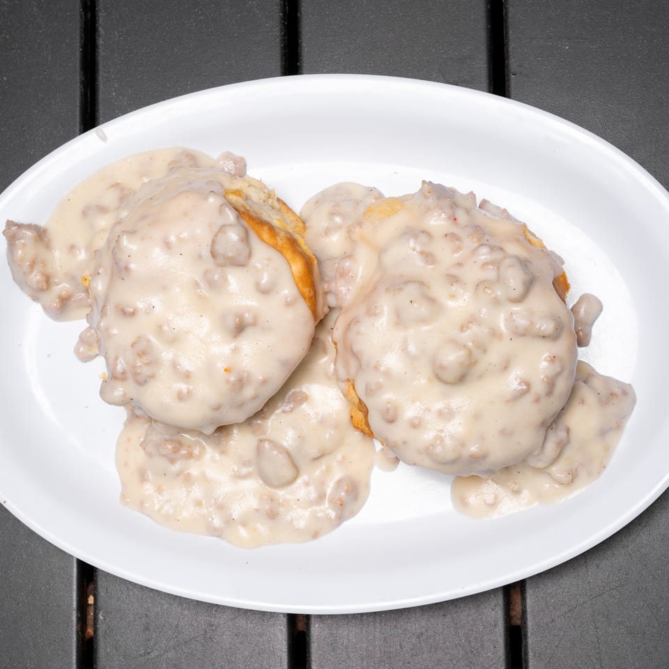Biscuits and gravy on a white oval plate, with a dark gray table in the background.