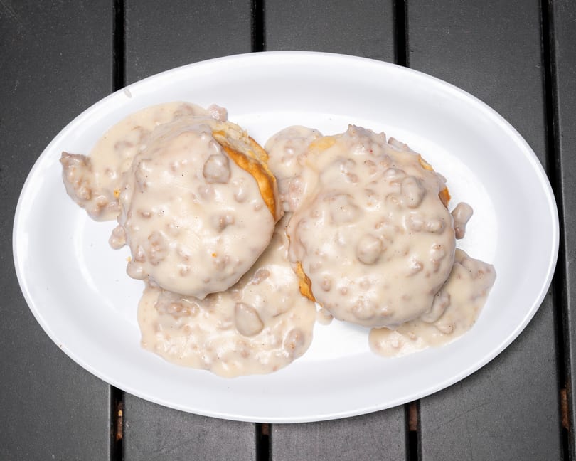 Biscuits and gravy on a white oval plate, with a dark gray table in the background.
