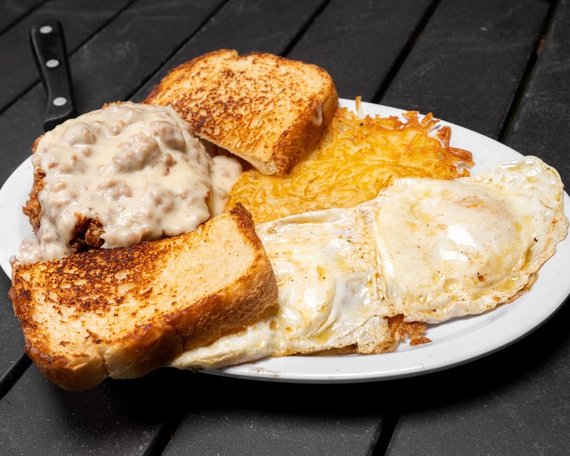 A breakfast plate with chicken fried steak, gravy, hash browns, fried eggs, and toast.