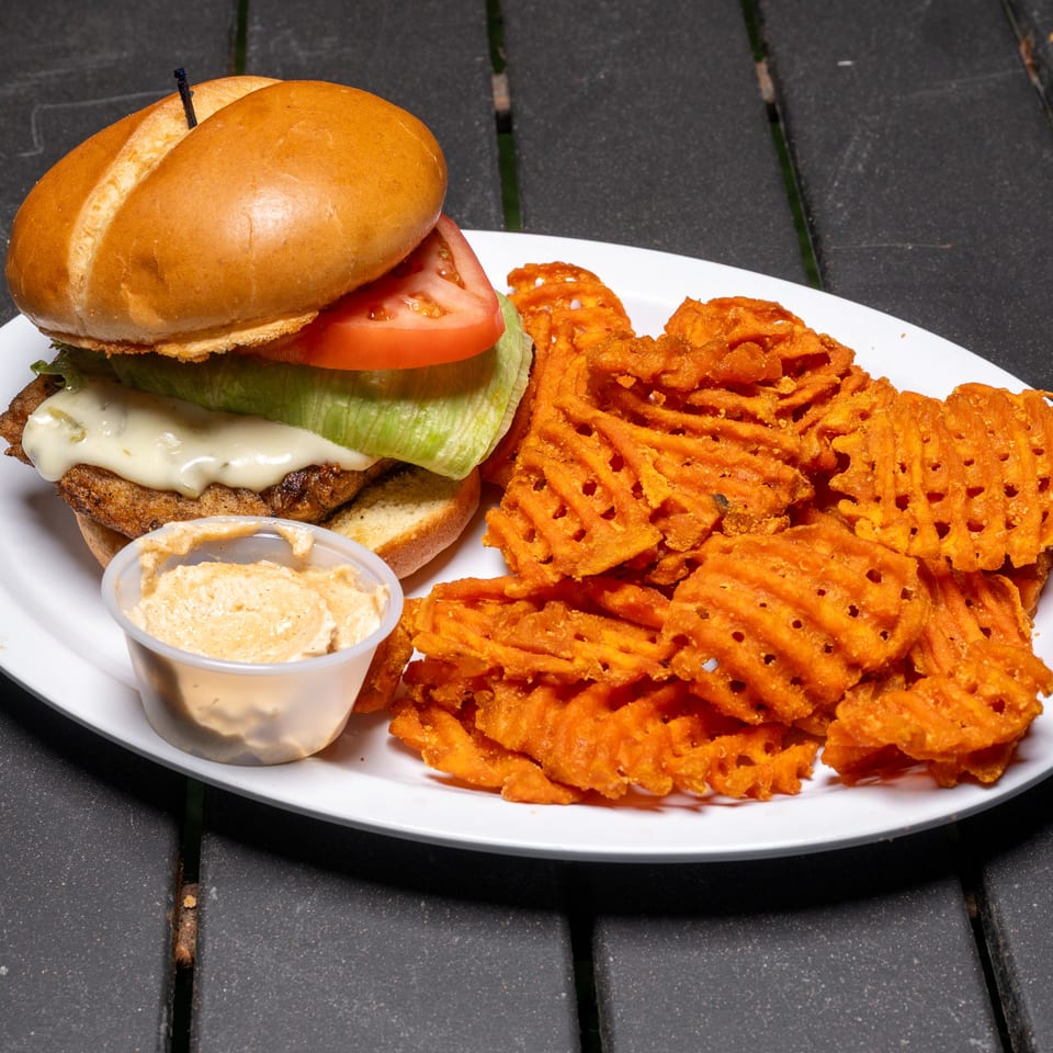 Chicken sandwich with melted cheese, lettuce, tomato, and a side of sweet potato waffle fries.