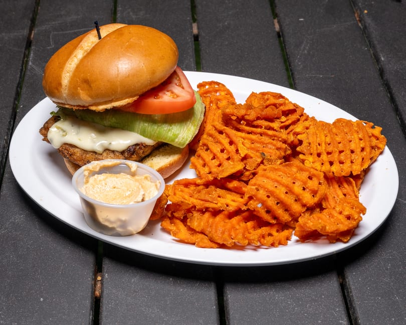 Chicken sandwich with melted cheese, lettuce, tomato, and a side of sweet potato waffle fries.