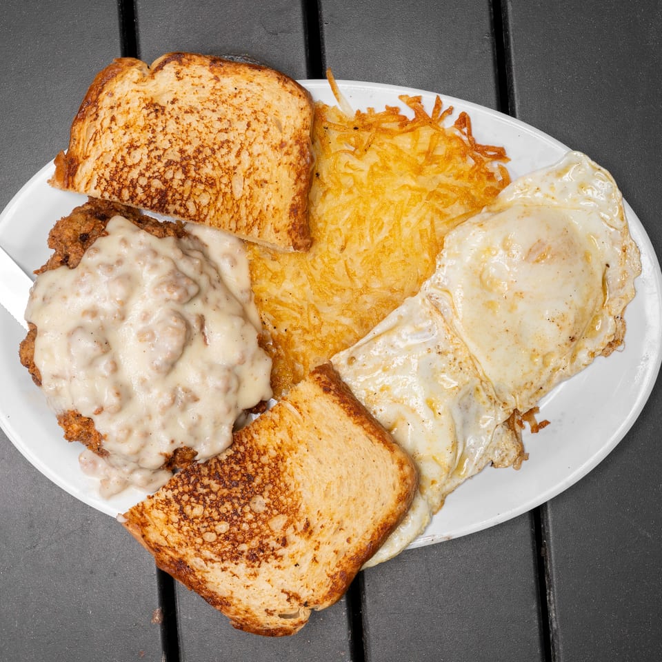 A breakfast plate with chicken fried steak and gravy, hash browns, fried eggs, and toast.