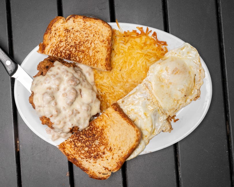 A breakfast plate with chicken fried steak and gravy, hash browns, fried eggs, and toast.