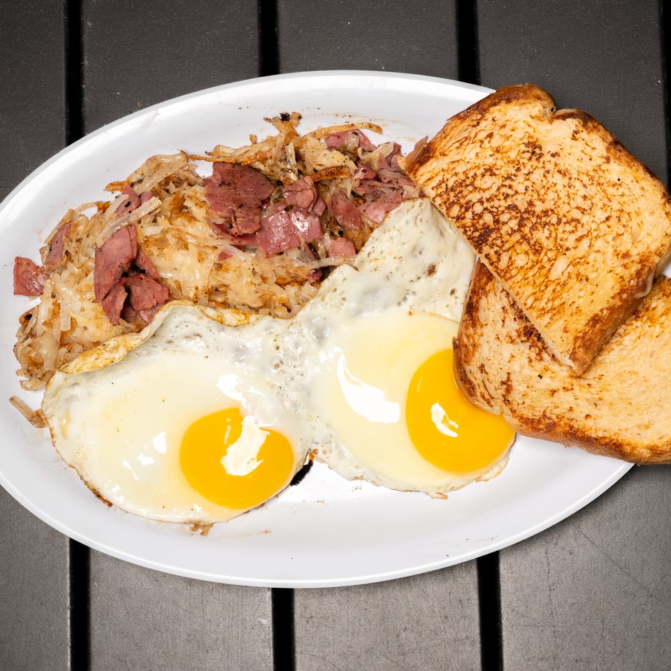 A breakfast plate with corned beef hash, two fried eggs, and two slices of toast.