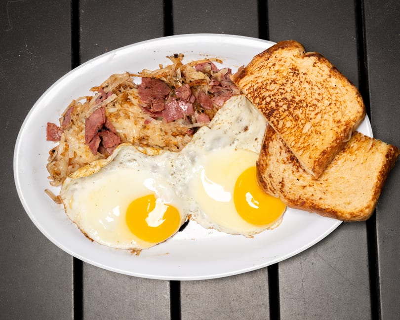 A breakfast plate with corned beef hash, two fried eggs, and two slices of toast.