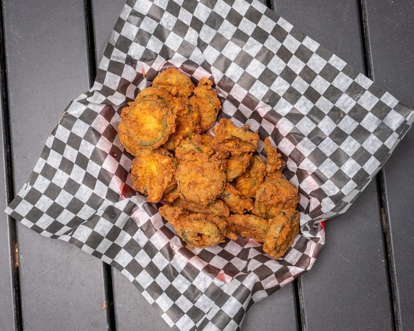 A basket of crispy fried pickles in a red basket lined with black and white checkered paper.