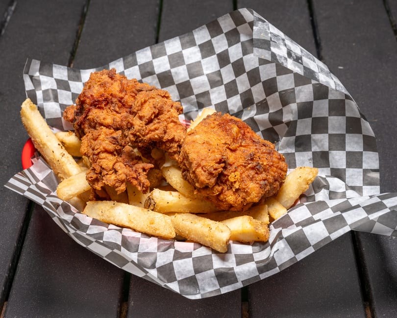 Crispy fried chicken pieces and thick-cut fries in a red basket with checkered paper lining.