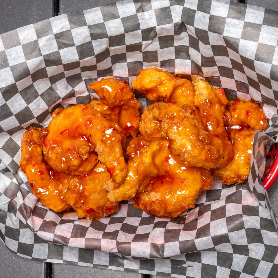 Sweet chili boneless wings in a red basket lined with black and white checkered paper.
