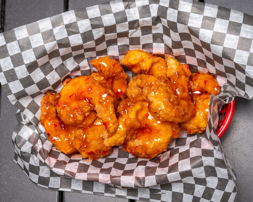 Sweet chili boneless wings in a red basket lined with black and white checkered paper.