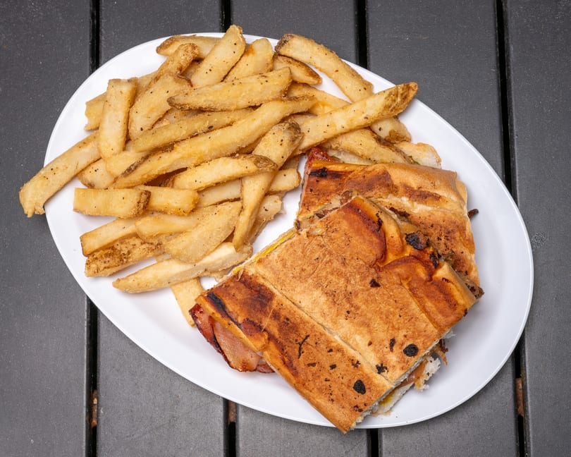 A Cuban sandwich cut in half with a side of french fries on a white plate.