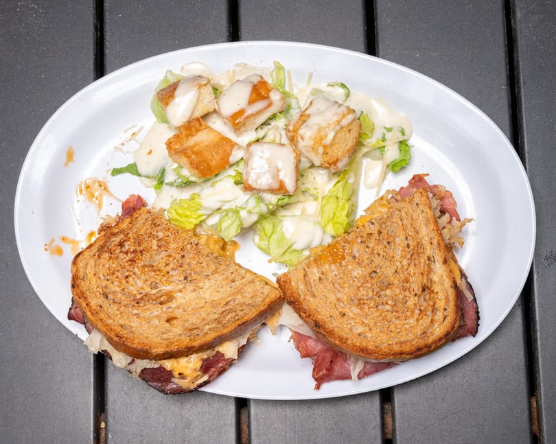 A reuben sandwich cut in half with a side of caesar salad on a white plate.